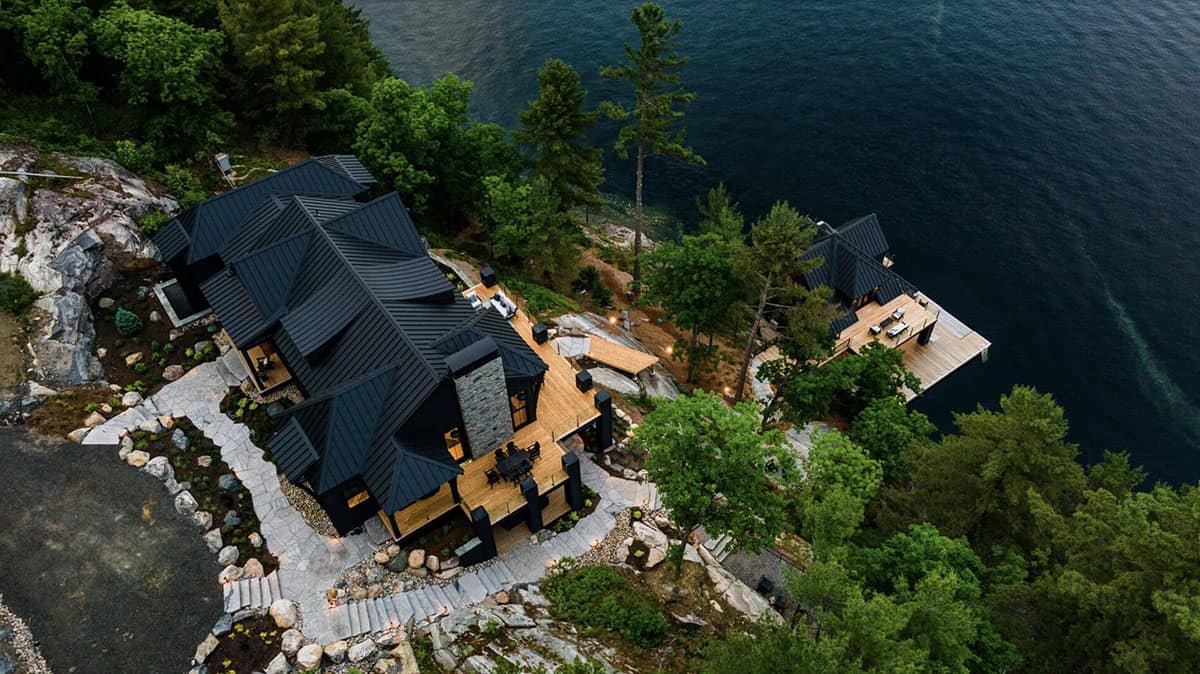 Twilight aerial of dark cottage and boathouse on rocky lakefront point with illuminated decks