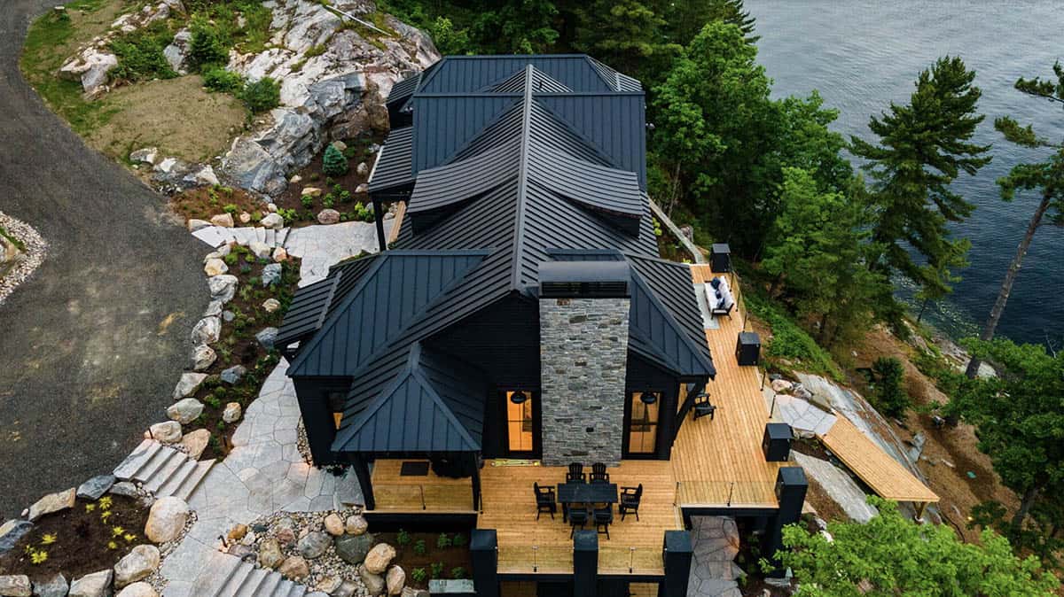 Overhead aerial of black standing seam metal roofline with stone chimney and wraparound cedar decks
