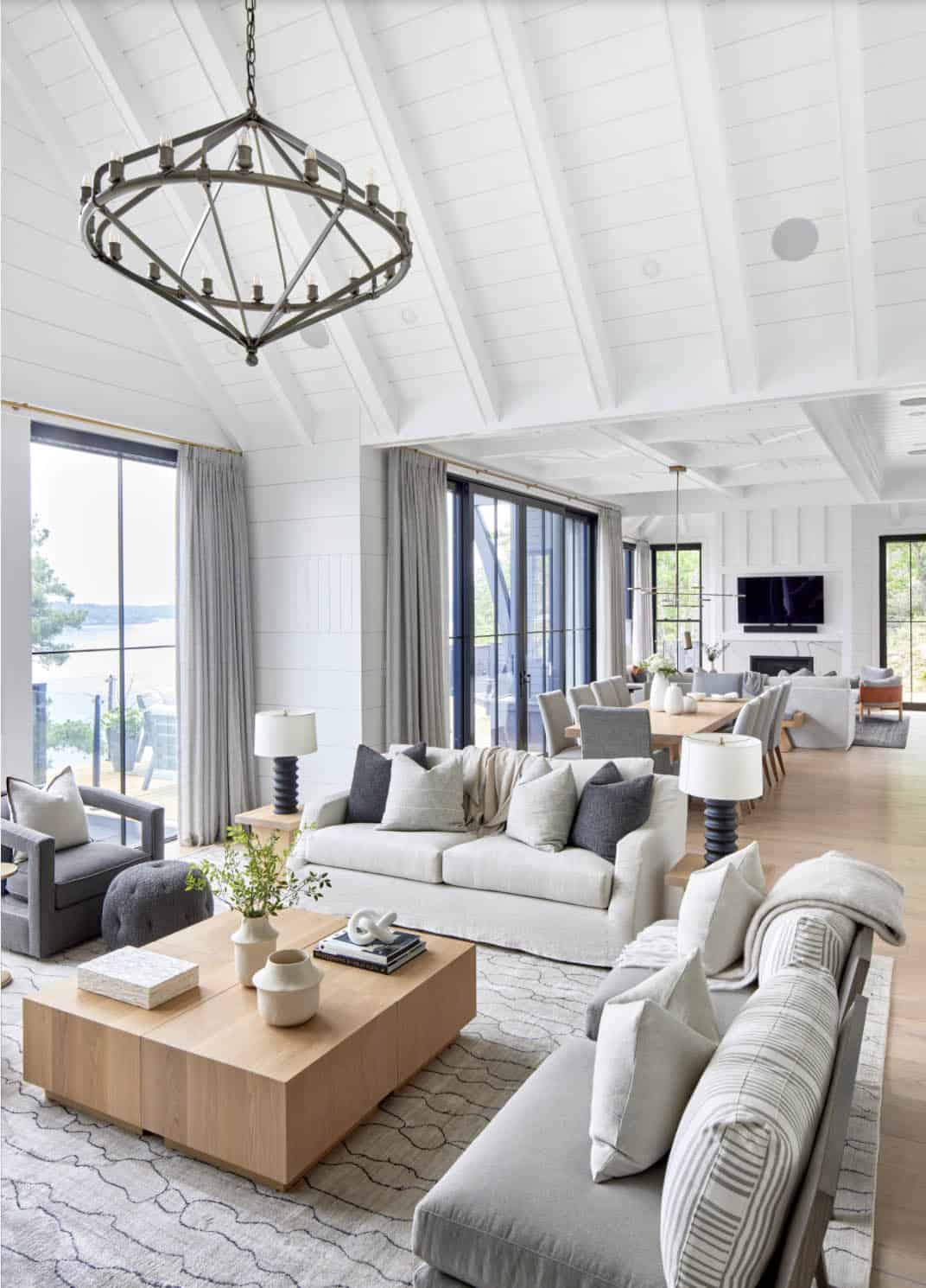 Open-plan cottage living room with cathedral ceiling, geometric chandelier, and lake-facing sliding doors