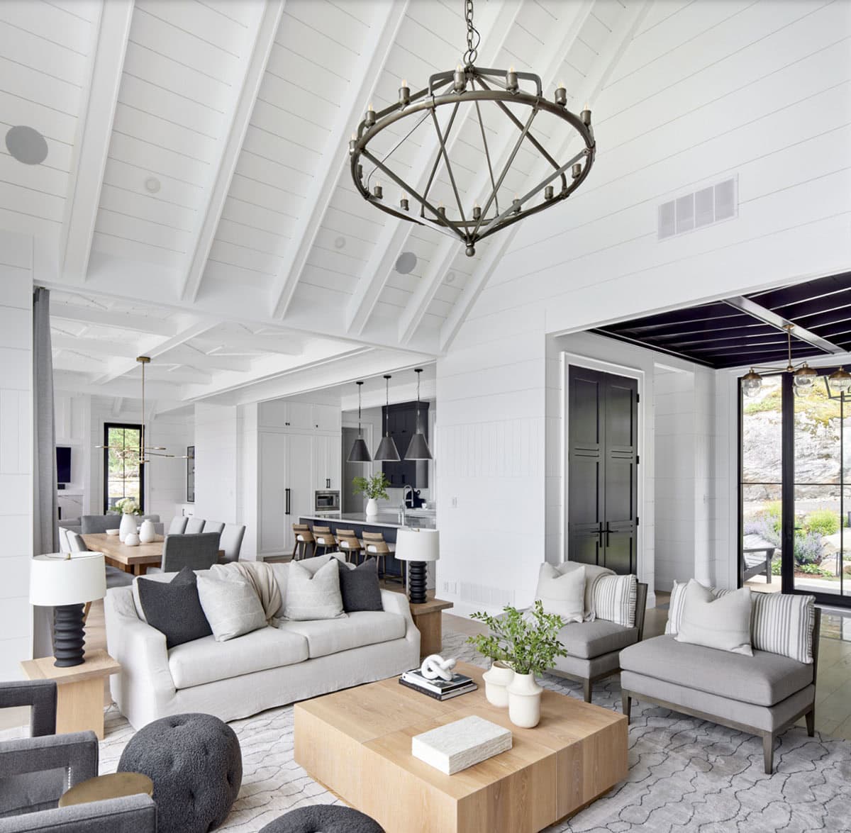Expansive open-plan living and dining area with white shiplap ceiling, iron chandelier, and kitchen beyond
