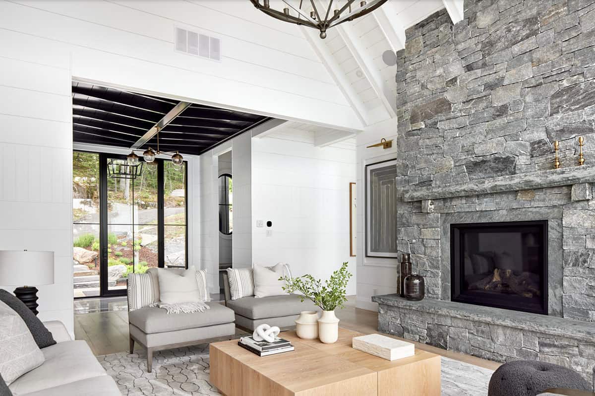 Cottage living room with tall stone fireplace, white vaulted ceiling, and contrasting dark sunroom entry