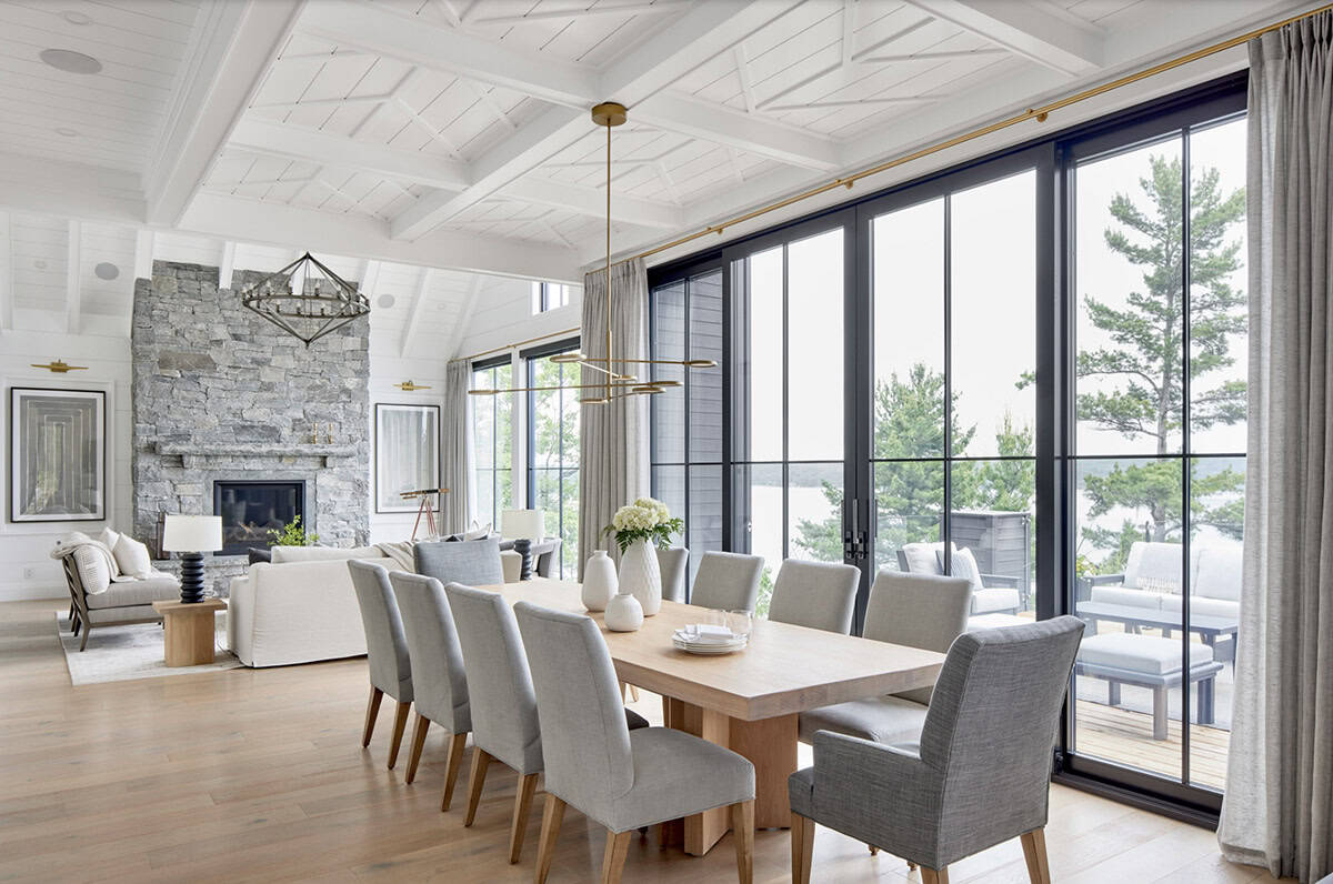 Open cottage dining room with oak table, stone fireplace, brass chandelier, and lake-view glass doors