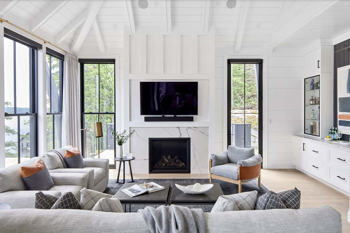 Lower-level family room with marble fireplace, TV, built-in bar, and floor-to-ceiling black-framed windows