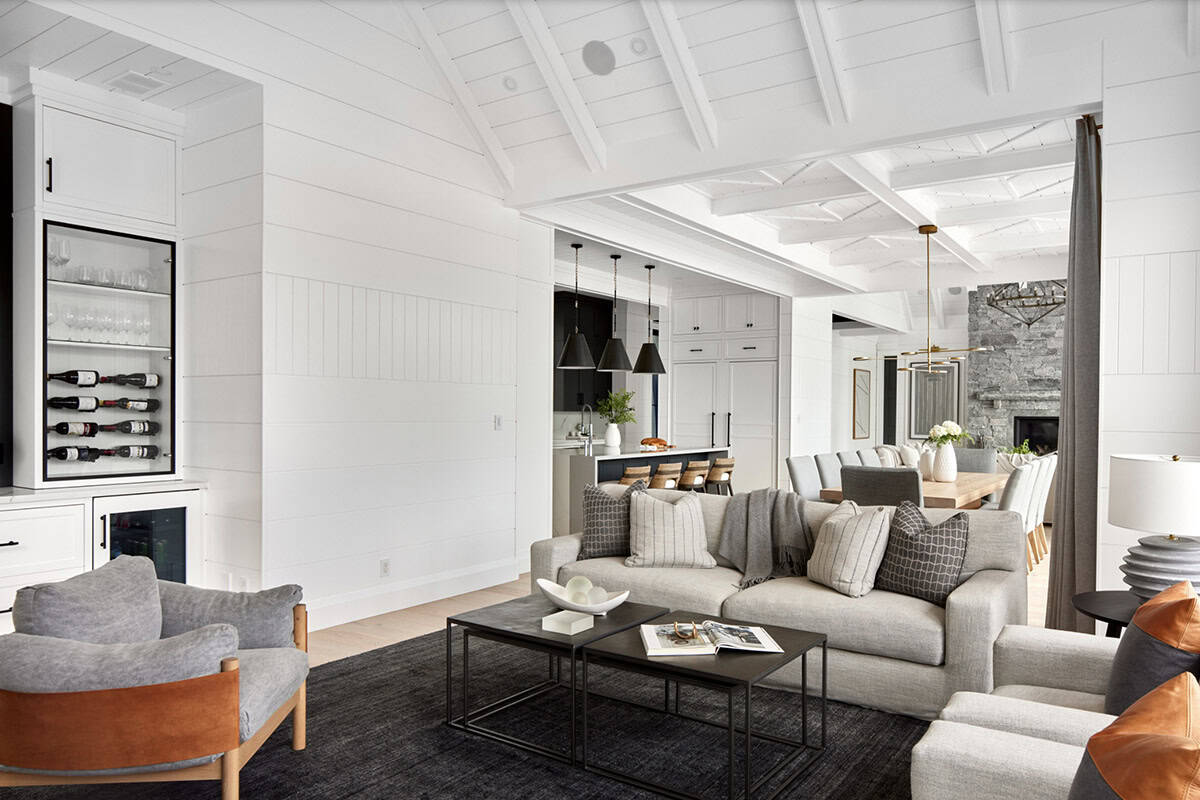 Cottage living room with built-in wine display, grey sofas, leather chairs, and open kitchen beyond