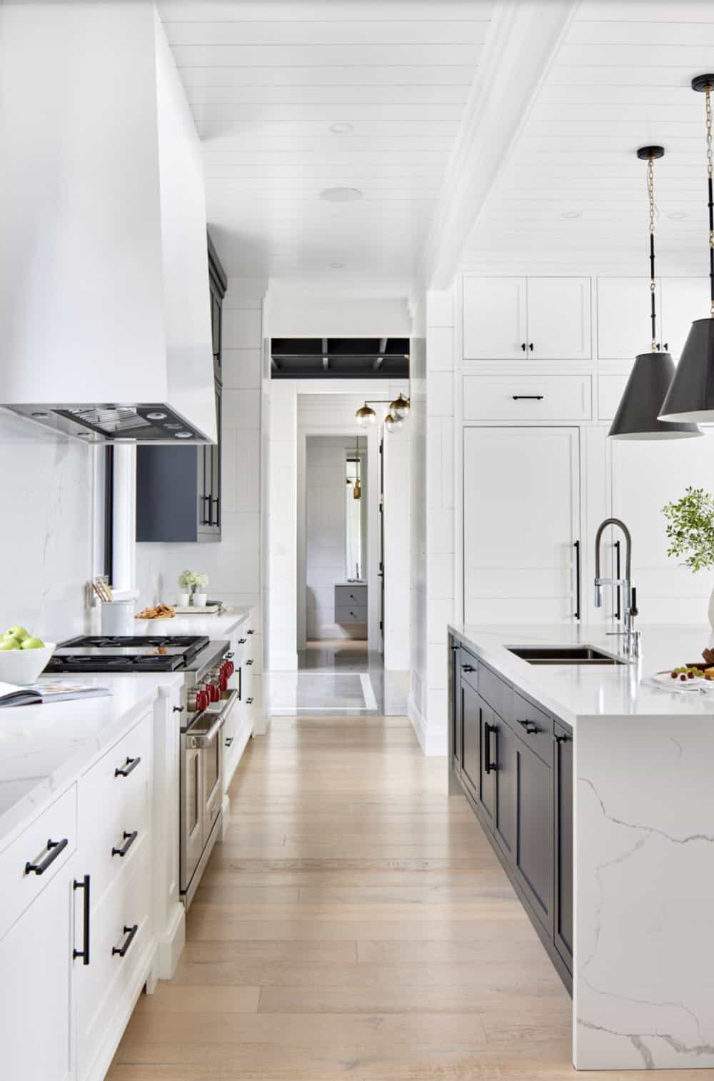 White kitchen with navy island, professional range, marble backsplash, and hallway to mudroom