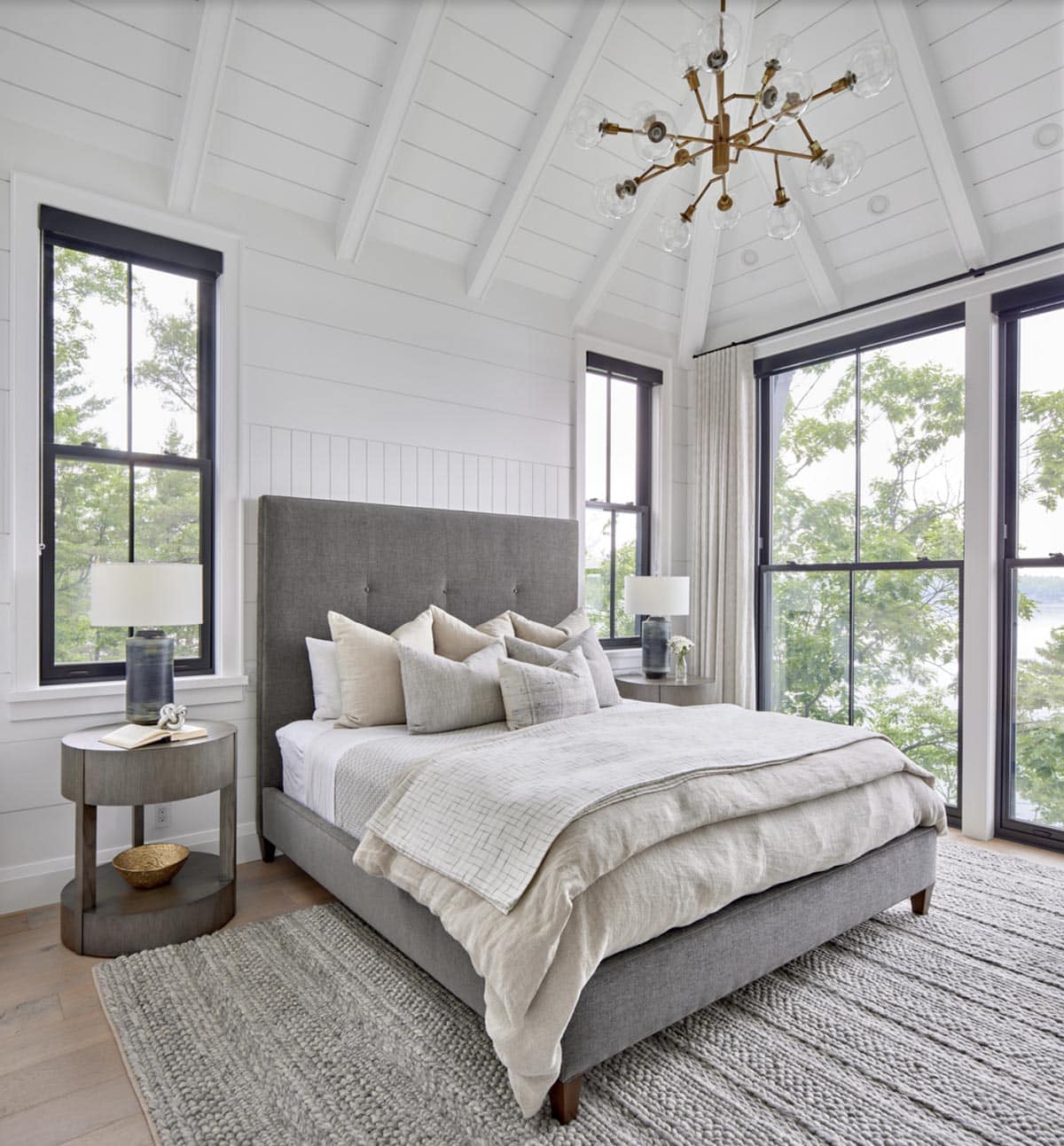 Primary bedroom with tufted grey headboard, cathedral shiplap ceiling, brass Sputnik chandelier, and lake views