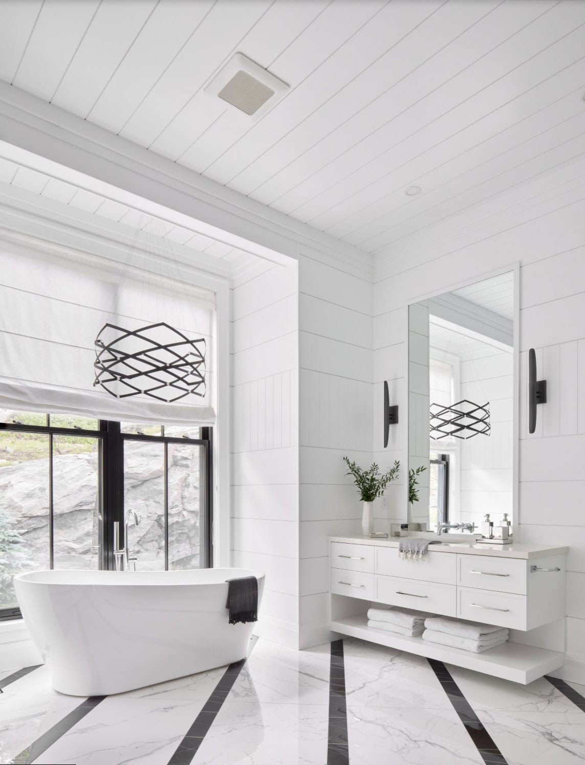 Primary ensuite with freestanding soaking tub, geometric black chandelier, and marble striped floor