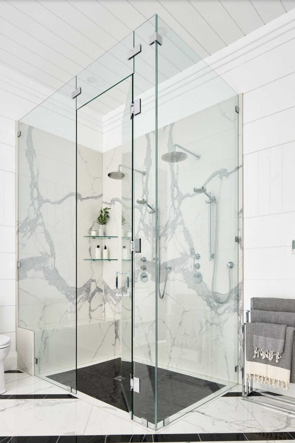 Frameless glass walk-in shower with dramatic marble slab walls and dual rain showerheads