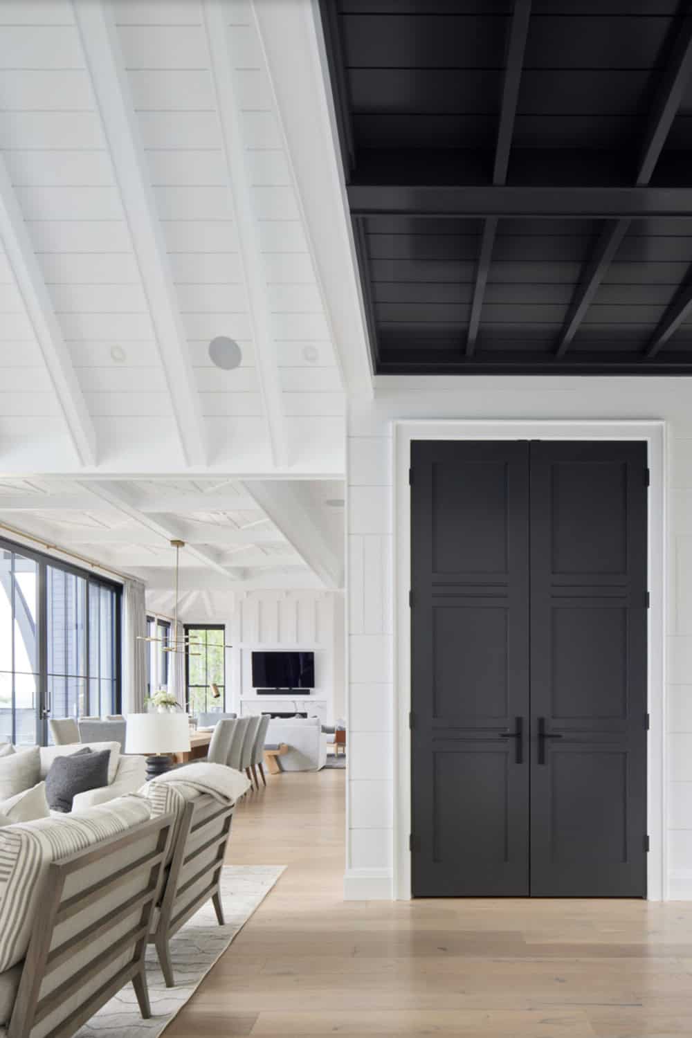 Interior hallway with contrast of white shiplap ceiling and dramatic black coffered ceiling beyond double doors