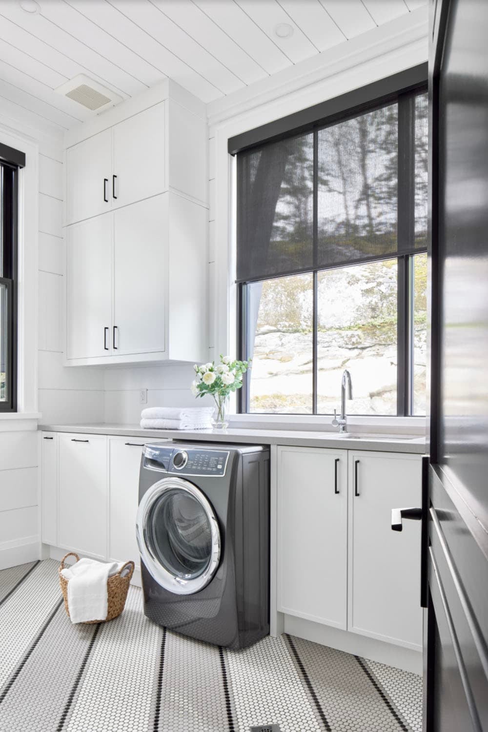 White laundry room with front-load washer, shaker cabinets, penny tile floor, and rock-view window