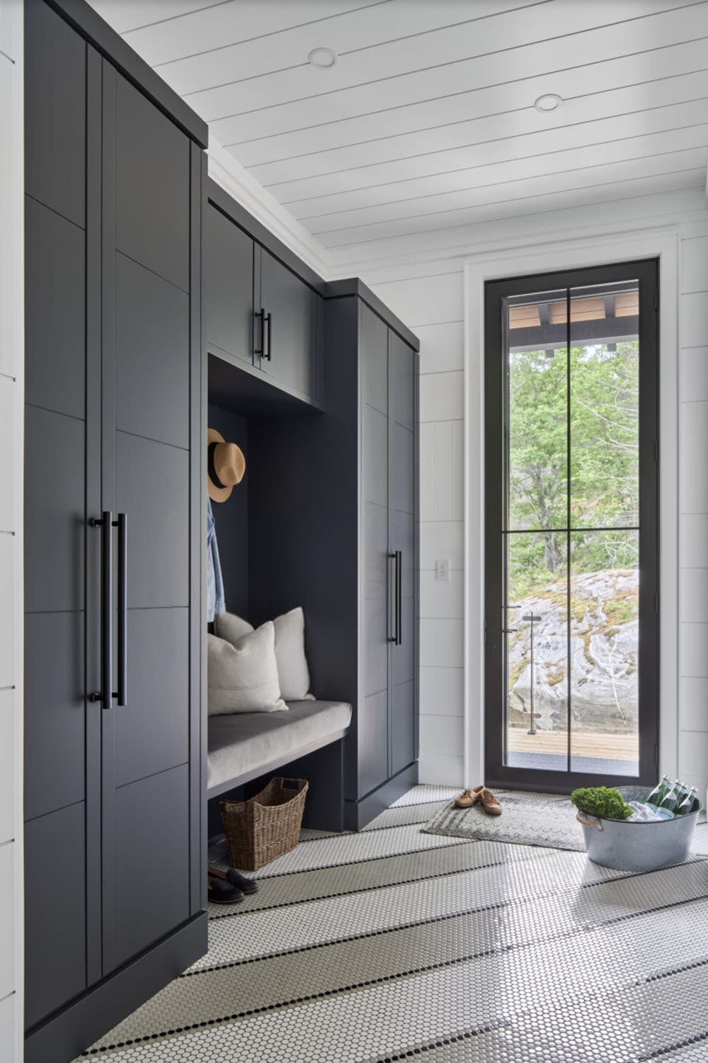 Dark navy mudroom with built-in lockers, bench seating, wicker basket, and tall black-framed window