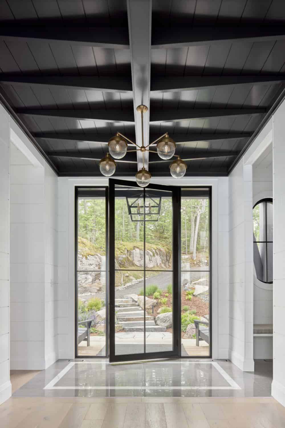 Dramatic foyer with black coffered ceiling, brass globe chandelier, and full-glass black-framed entry door