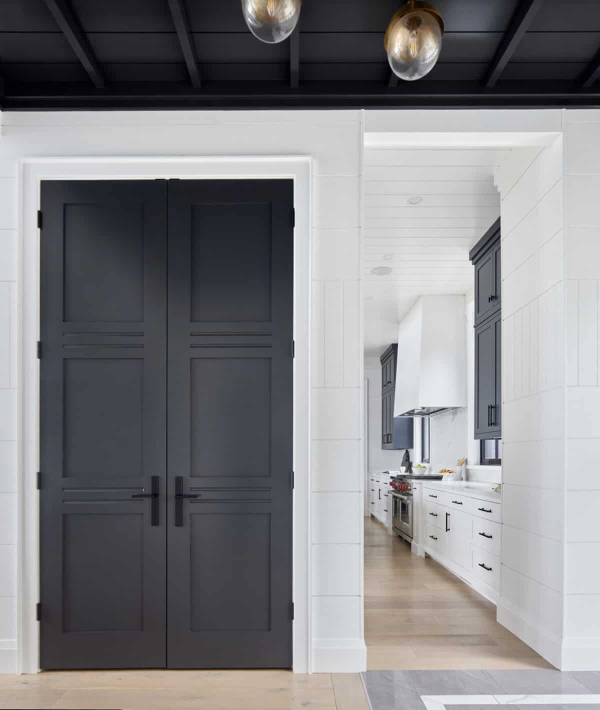 Vestibule with tall black double doors, black coffered ceiling, globe pendants, and view to navy kitchen