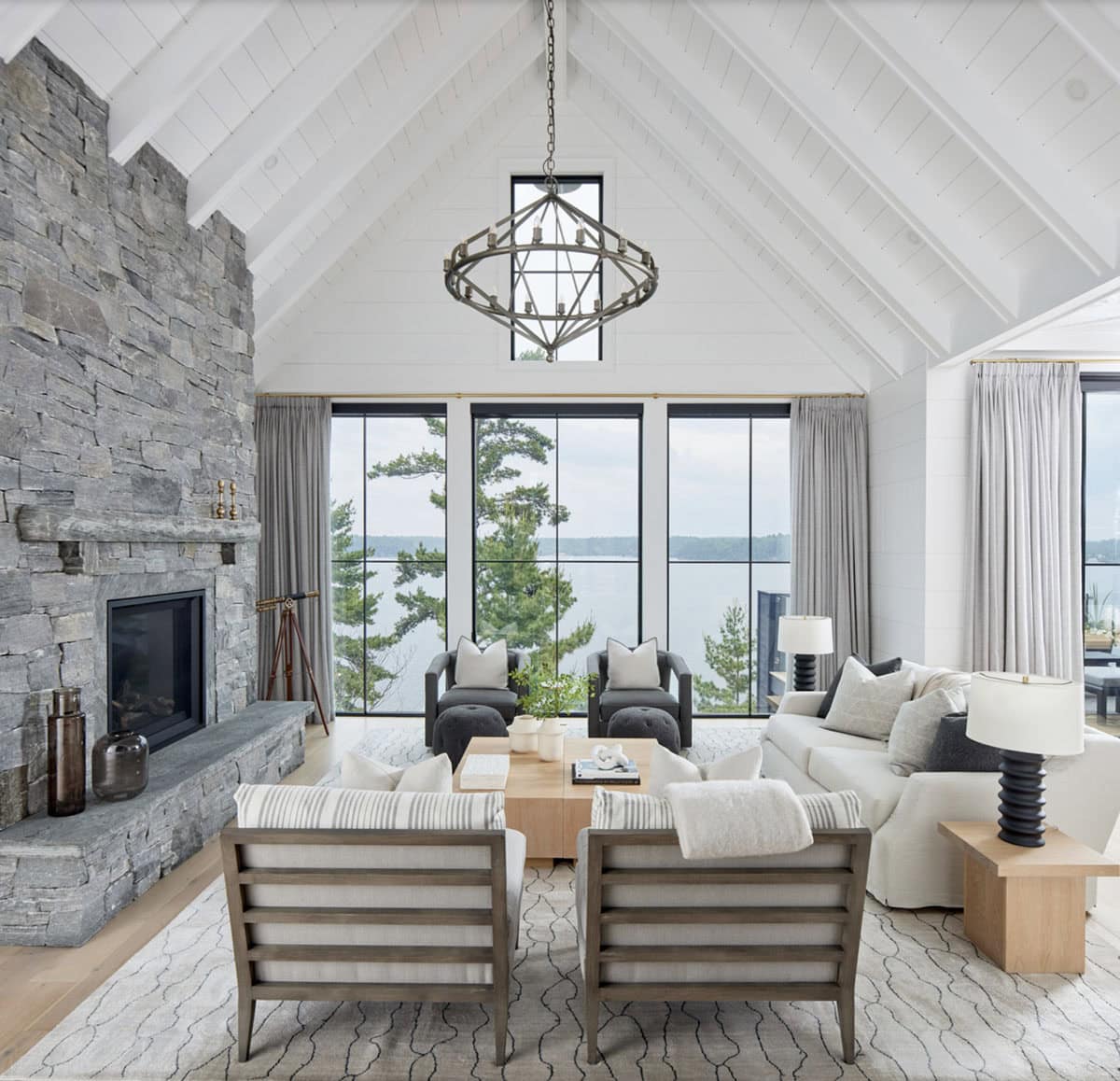 Cottage great room with floor-to-ceiling stone fireplace, geometric chandelier, and panoramic lake windows