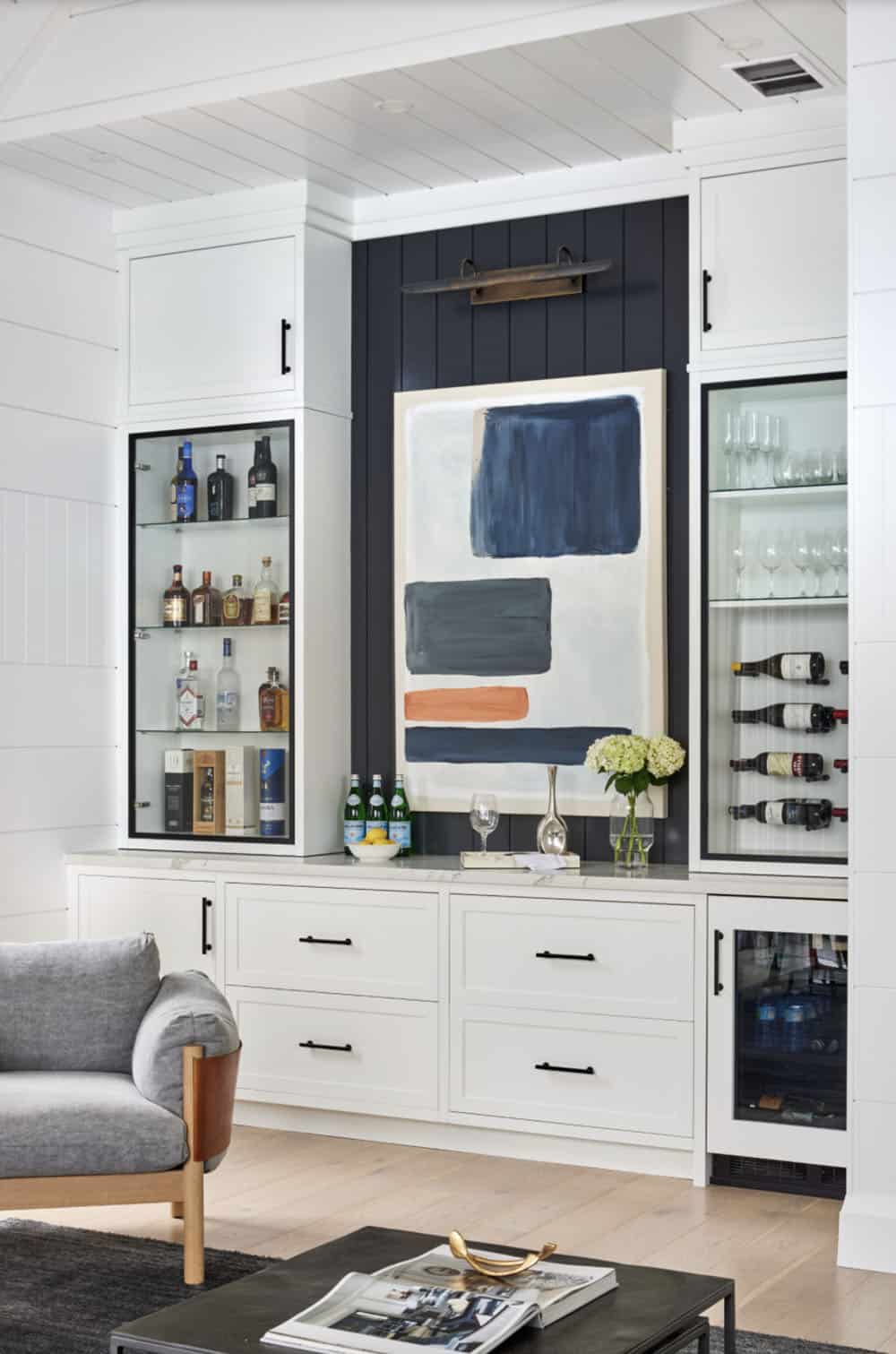 Built-in wet bar with liquor display cabinet, wine rack, abstract blue artwork, and navy shiplap accent wall