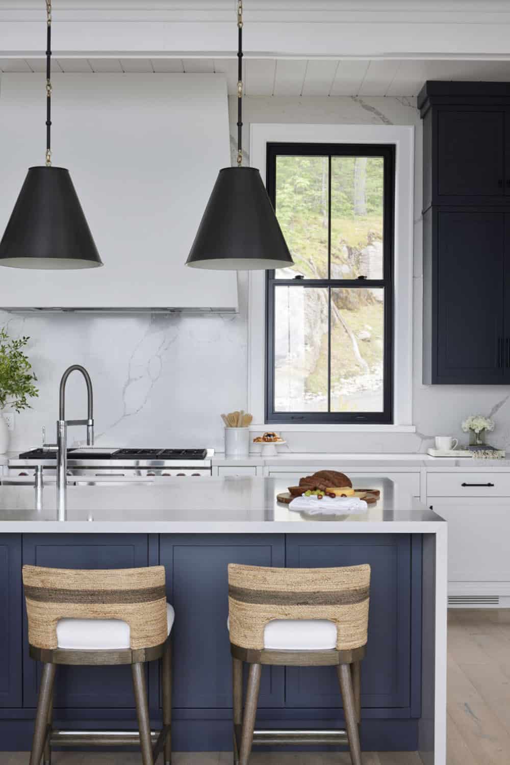 Navy kitchen island with two woven barstools, black cone pendants, and marble backsplash