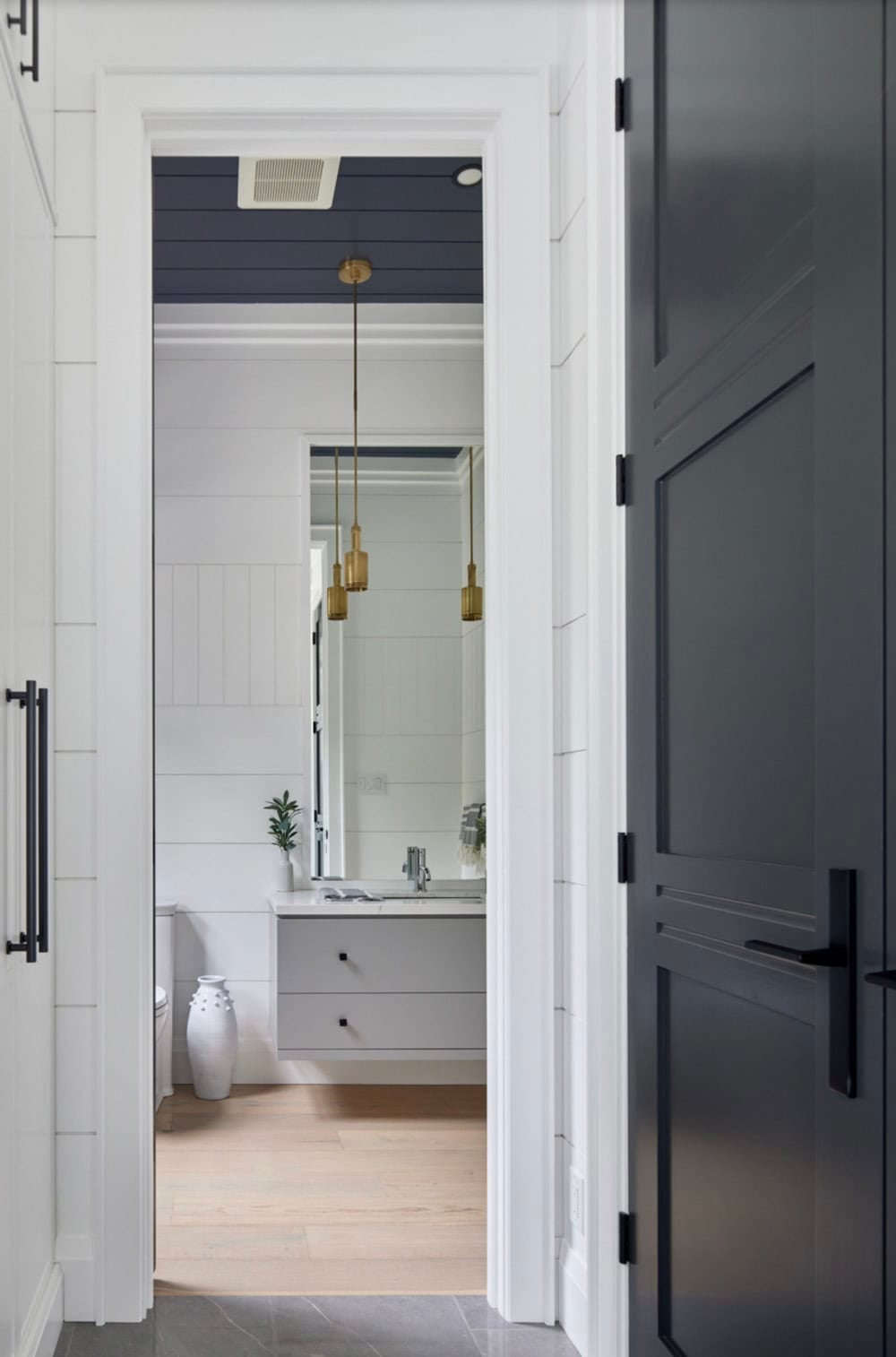 View through dark door into powder room with navy ceiling, brass pendant lights, and grey floating vanity