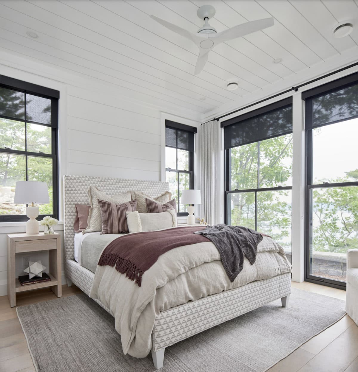 Guest bedroom with patterned upholstered bed, burgundy throw, white ceiling fan, and lake-view windows