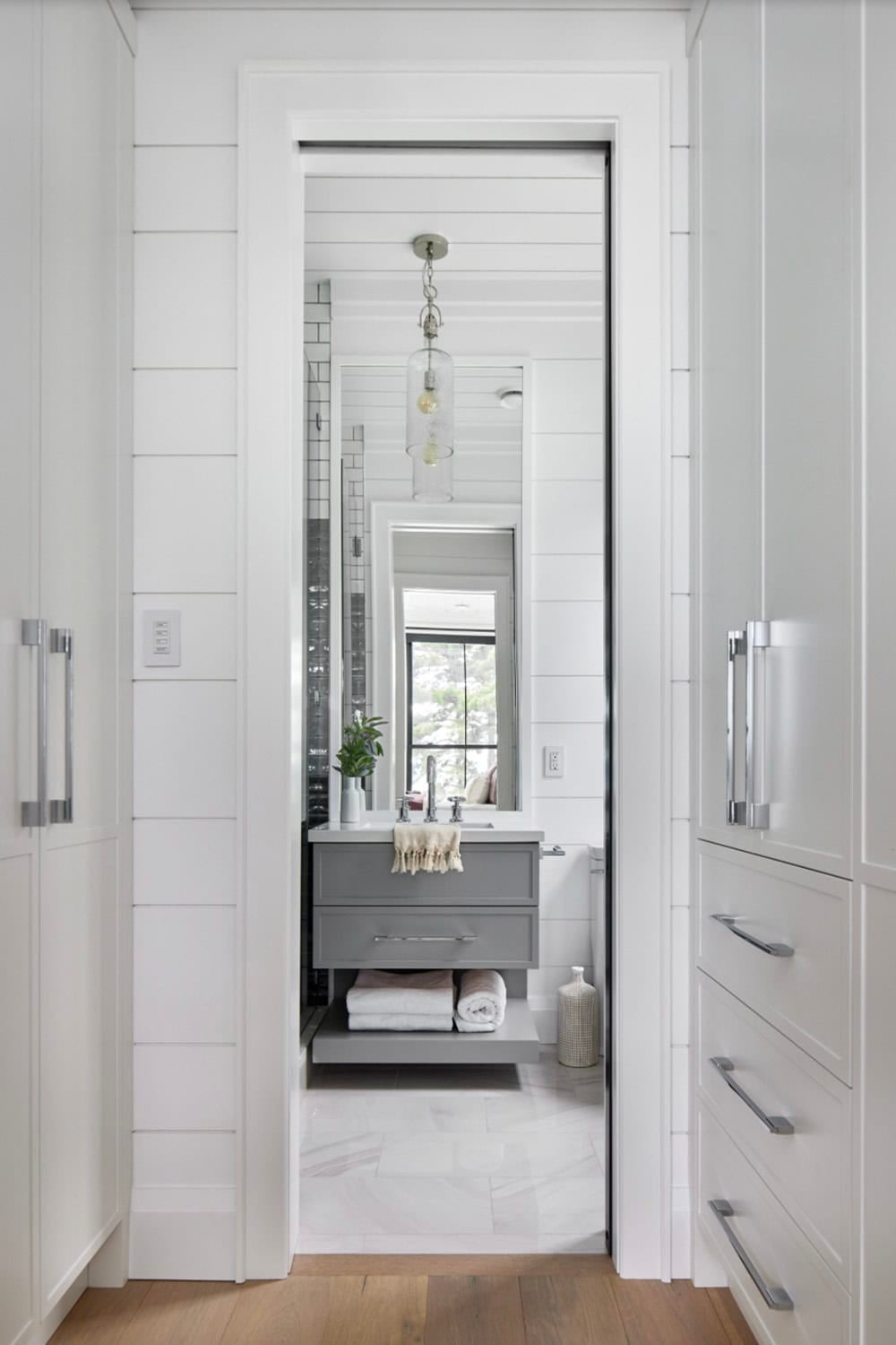 Ensuite glimpsed through pocket door showing grey floating vanity, glass pendant, and white subway tile