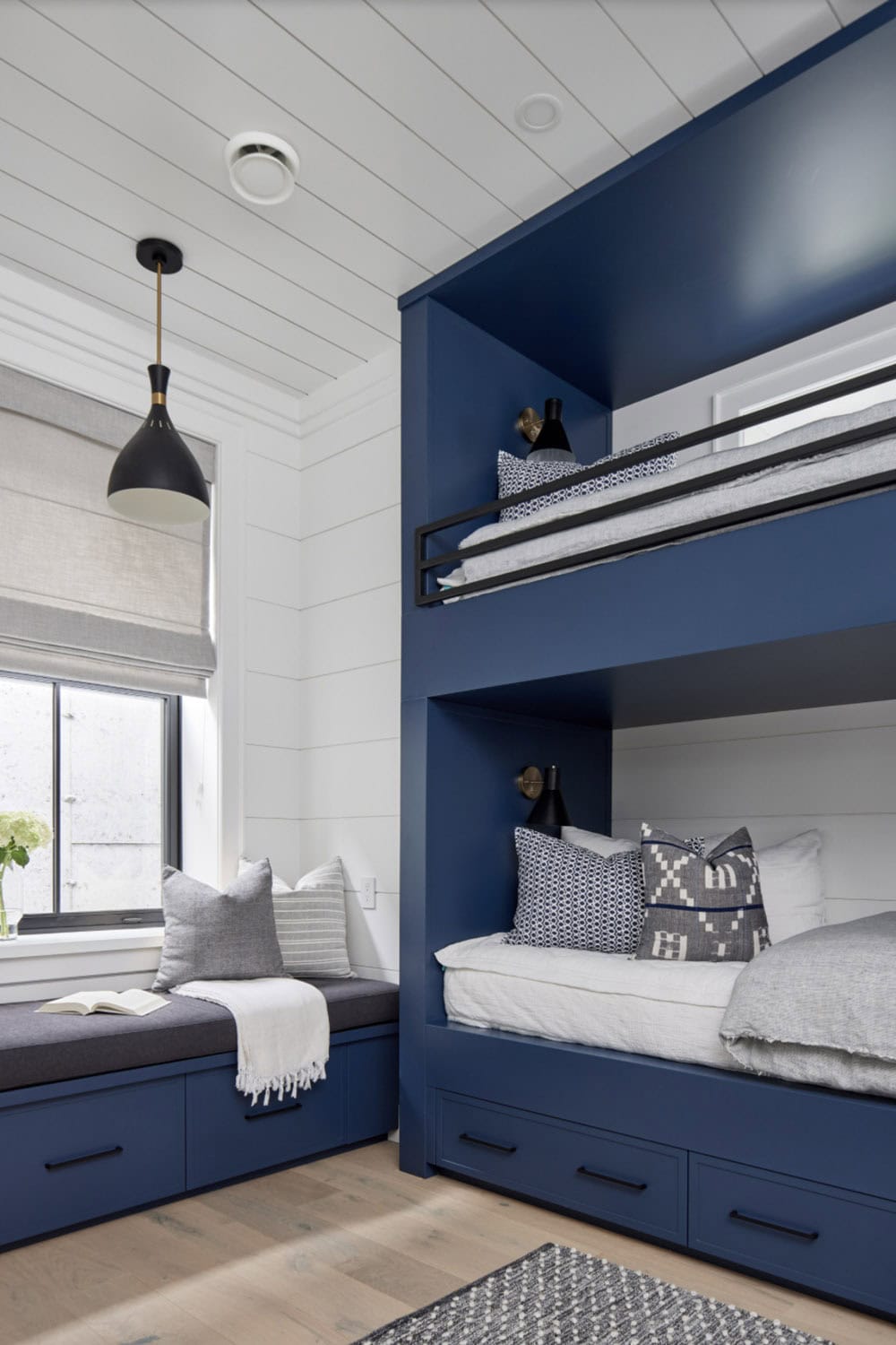 Navy bunk bed nook with black iron ladder, patterned pillows, and built-in storage drawers below