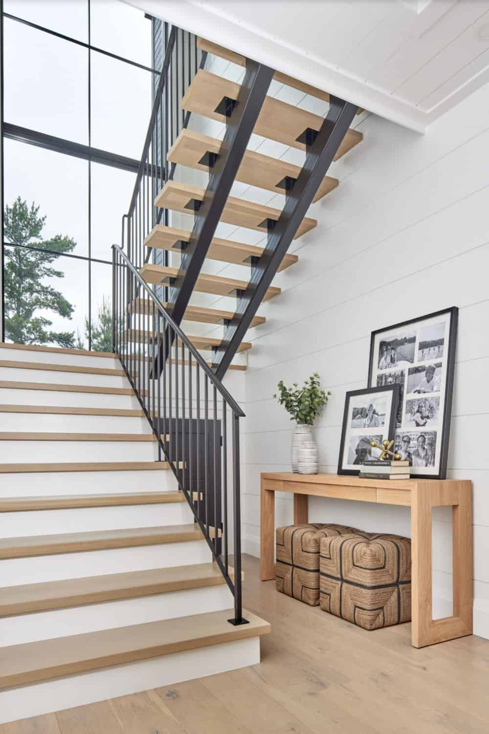 White oak open-riser staircase with black iron railing, tall window backdrop, and oak console table