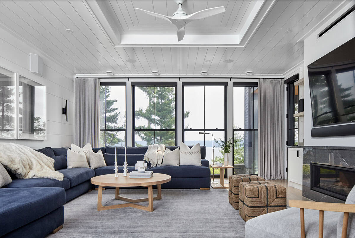Lower-level living room with navy sectional, round oak coffee table, woven ottomans, and lake windows