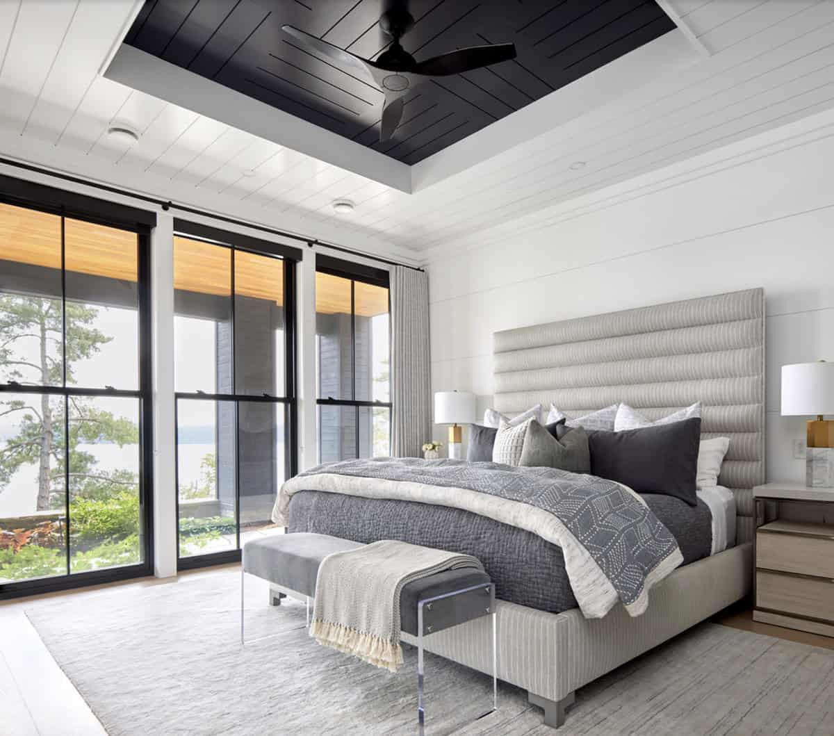 Primary bedroom with channeled headboard, black tray ceiling, lake-view sliding doors, and acrylic bench