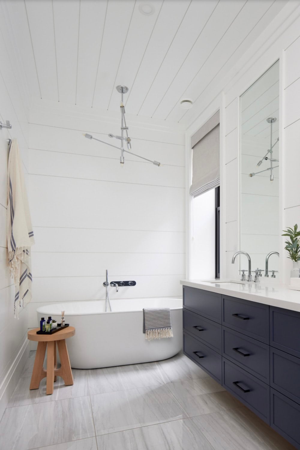 Ensuite with freestanding soaking tub, navy floating vanity, chrome Sputnik chandelier, and shiplap walls