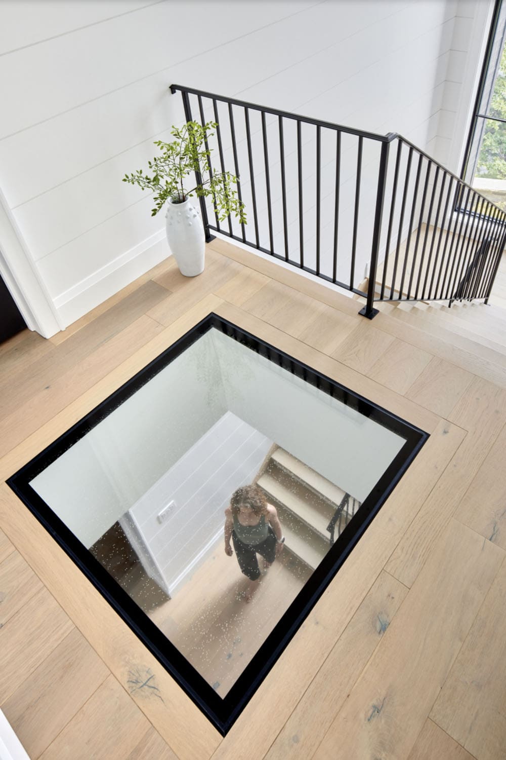 Upper hallway looking down through glass floor panel at person ascending stairs below