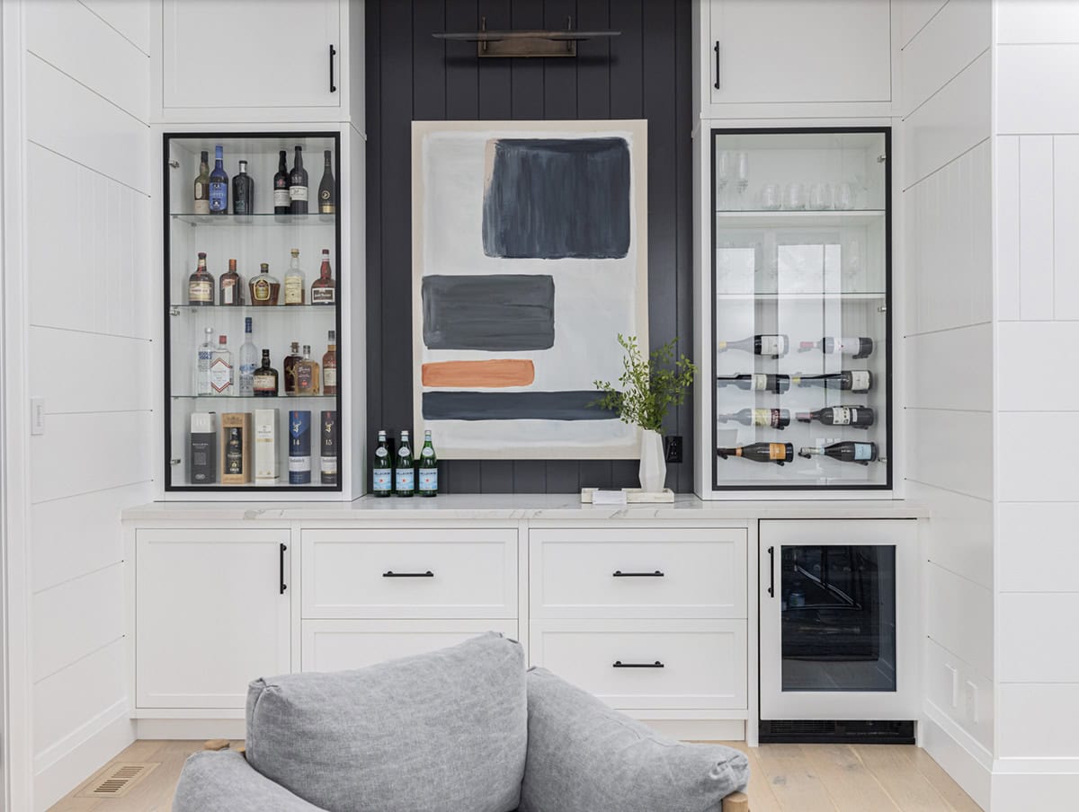 Built-in bar with glass liquor cabinet, wall-mounted wine rack, abstract artwork, and navy shiplap accent
