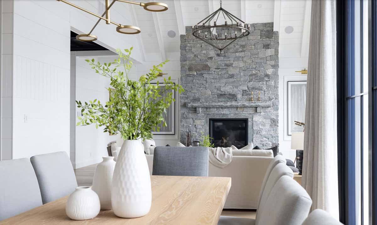 Dining table centerpiece with white ceramic vases and greenery framing the stone fireplace beyond