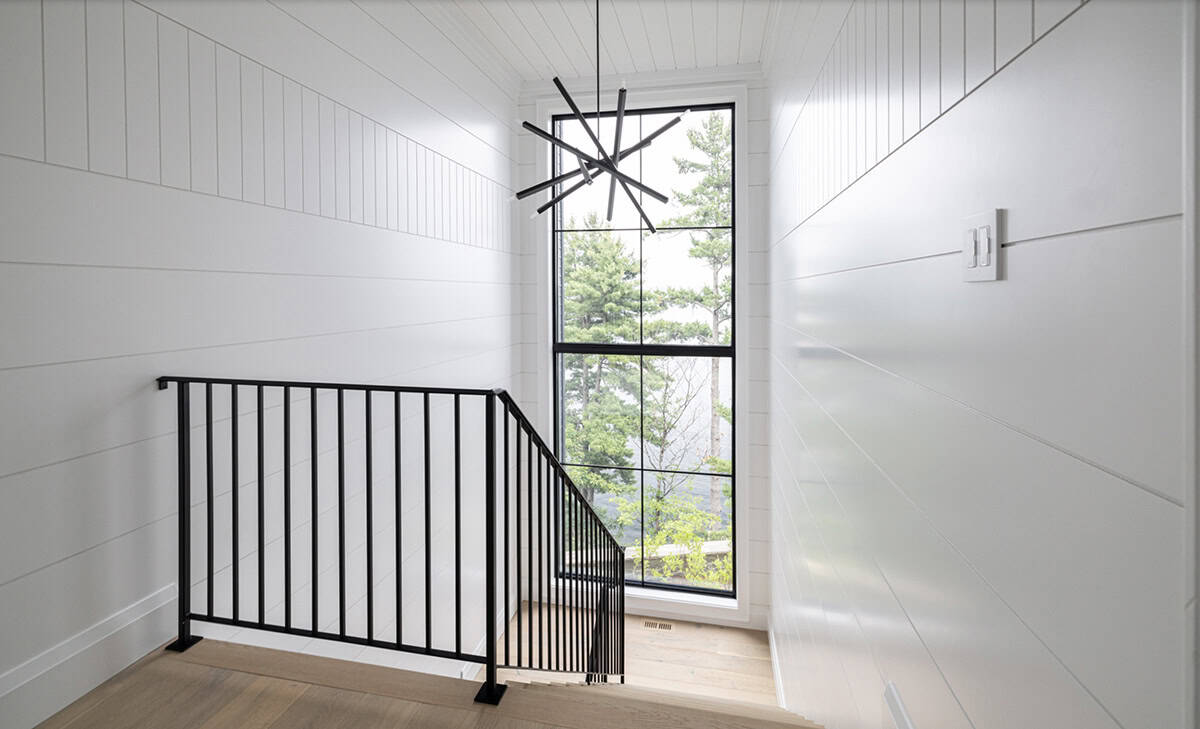 Staircase landing with white shiplap walls, black iron railing, starburst chandelier, and tall window