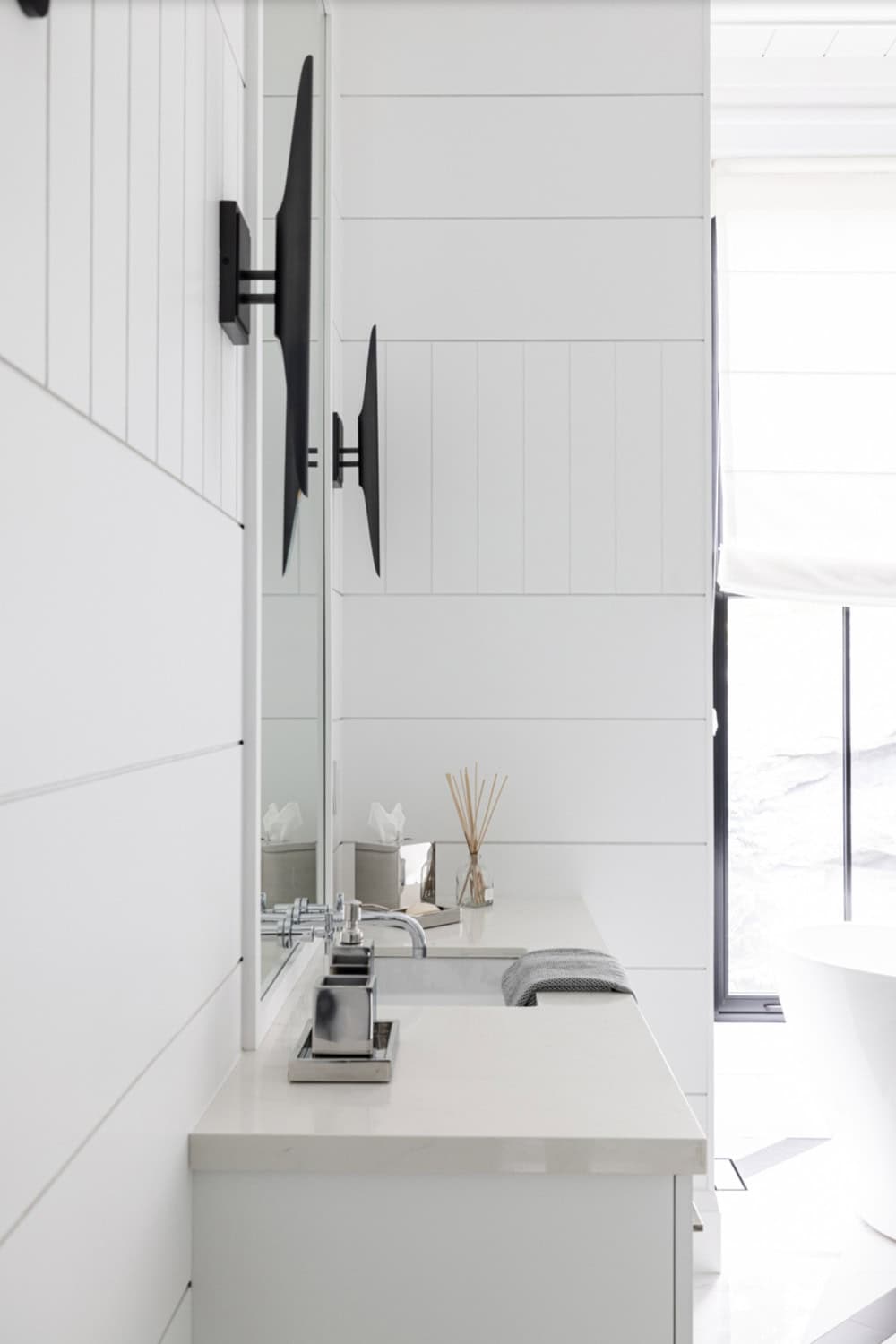 Primary ensuite vanity detail with white quartz countertop, chrome faucet, and black wall-mount sconces