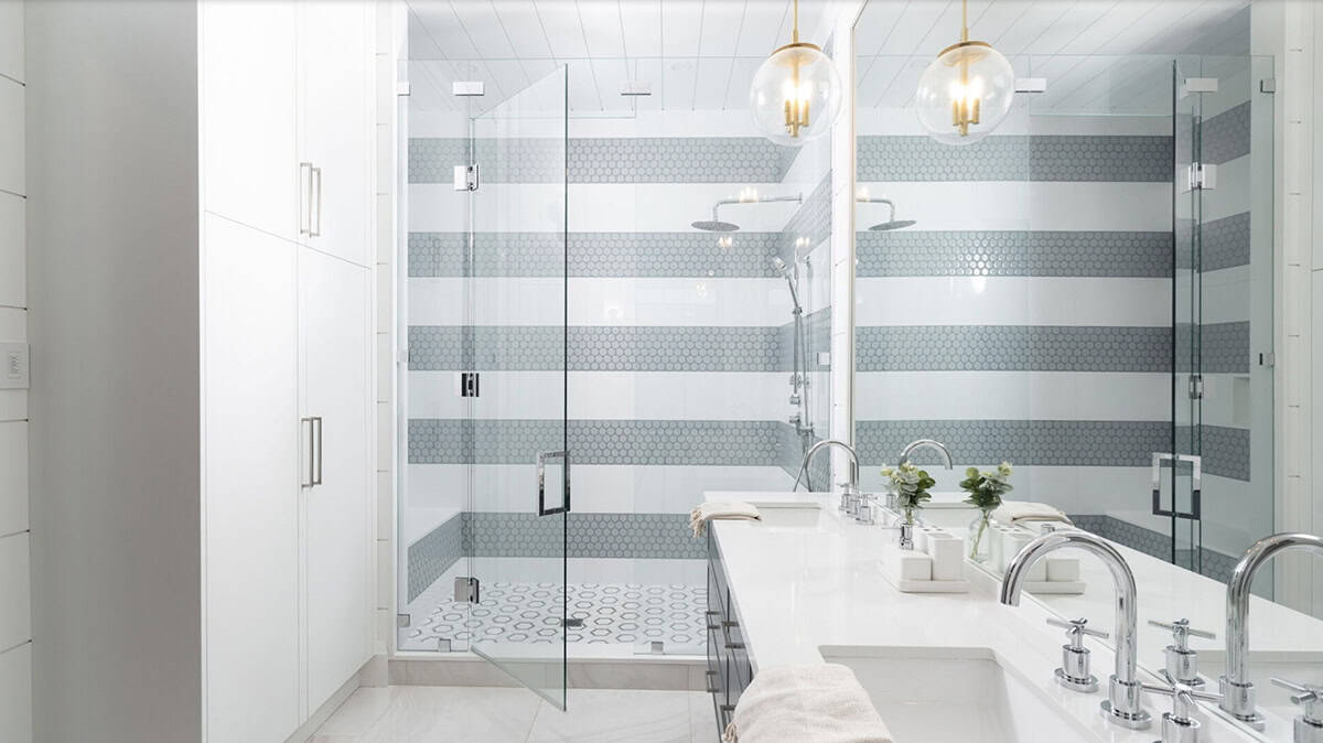 Jack-and-jill bathroom with striped penny tile shower, glass enclosure, double white vanity, and brass globe pendants