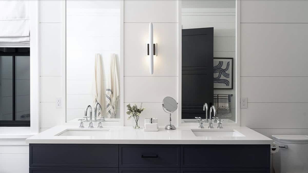 Navy double vanity with white quartz countertop, dual chrome faucets, and slim tubular wall sconce