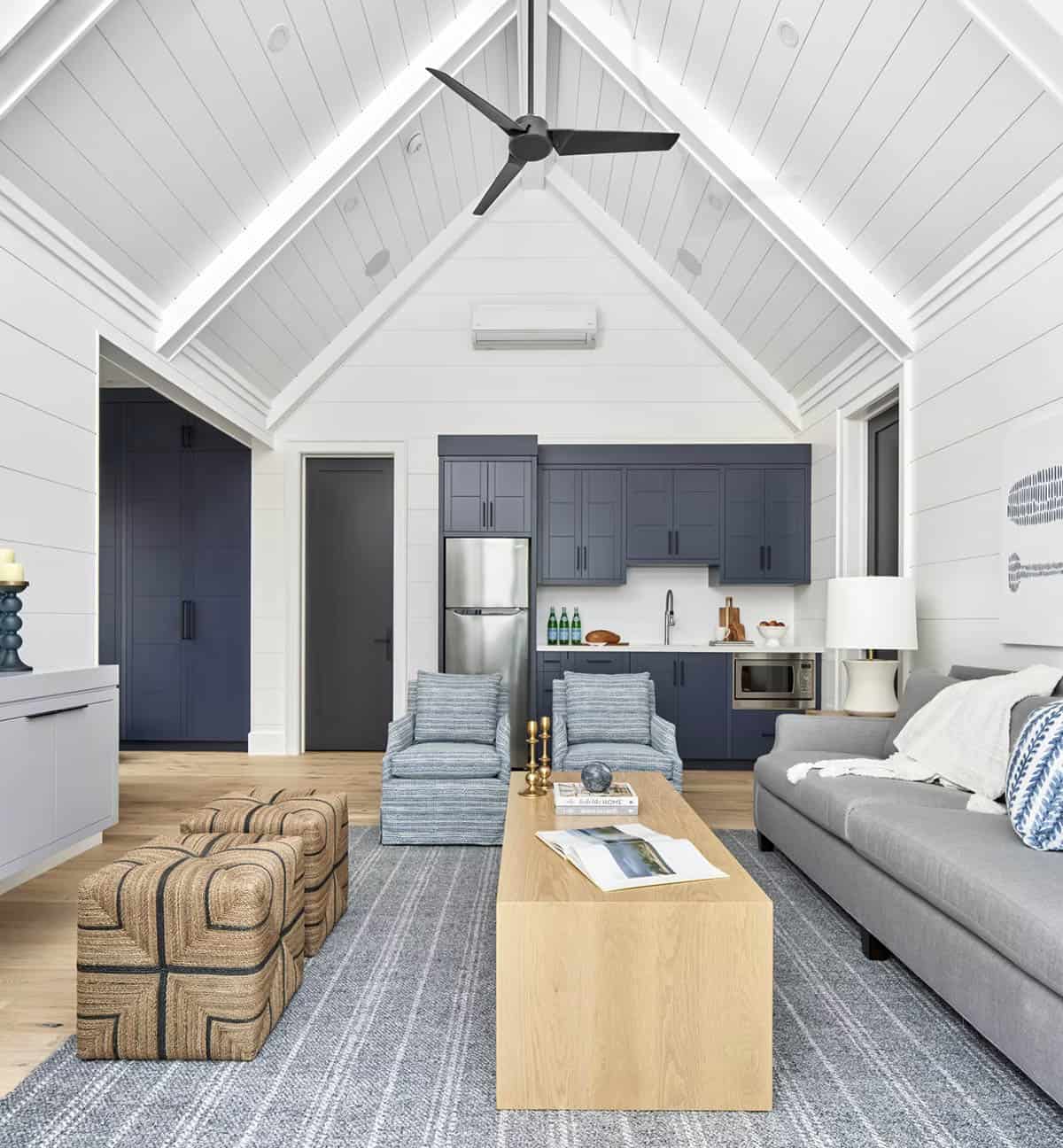Boathouse great room with navy blue kitchenette, blue patterned armchairs, jute ottomans, and white shiplap walls