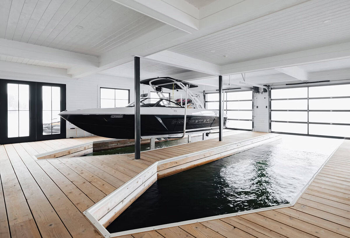 Indoor boat slip with wood dock flooring, black steel lift posts, and glass garage doors