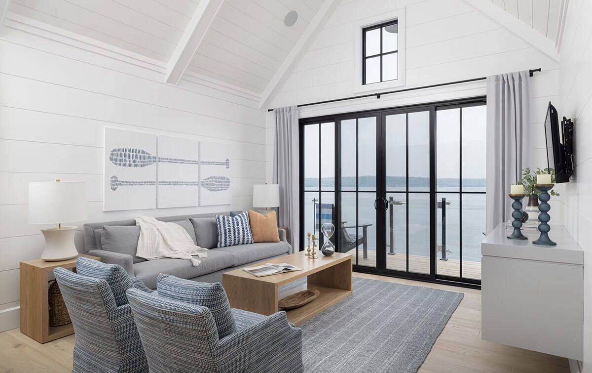Boathouse living area with gray sofa, paddle artwork, and sliding glass doors opening to lake deck