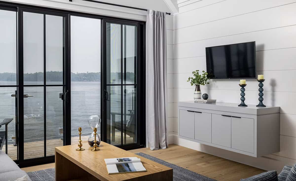 Boathouse living room detail showing wall-mounted TV, floating gray media cabinet, and lake views