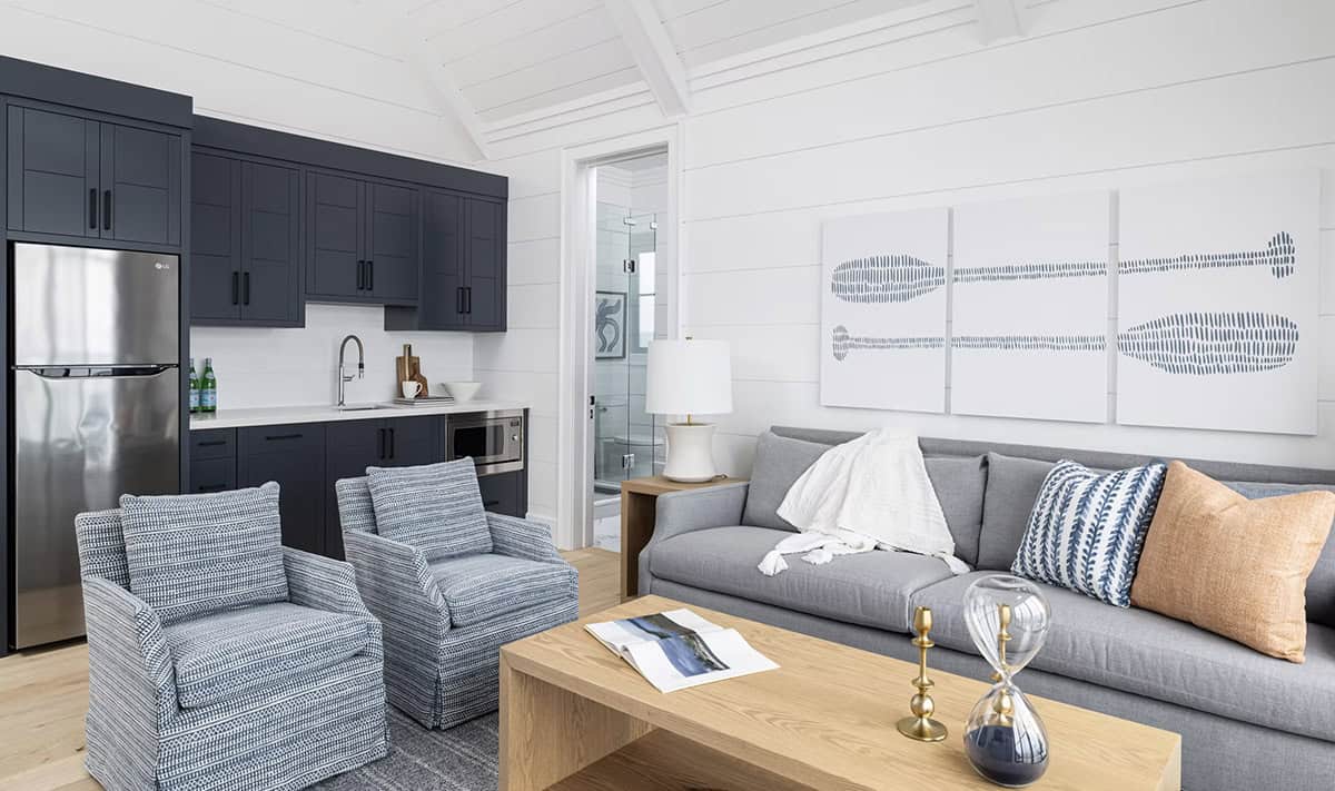 Boathouse open-plan living and kitchenette with navy cabinetry, blue armchairs, and paddle wall art