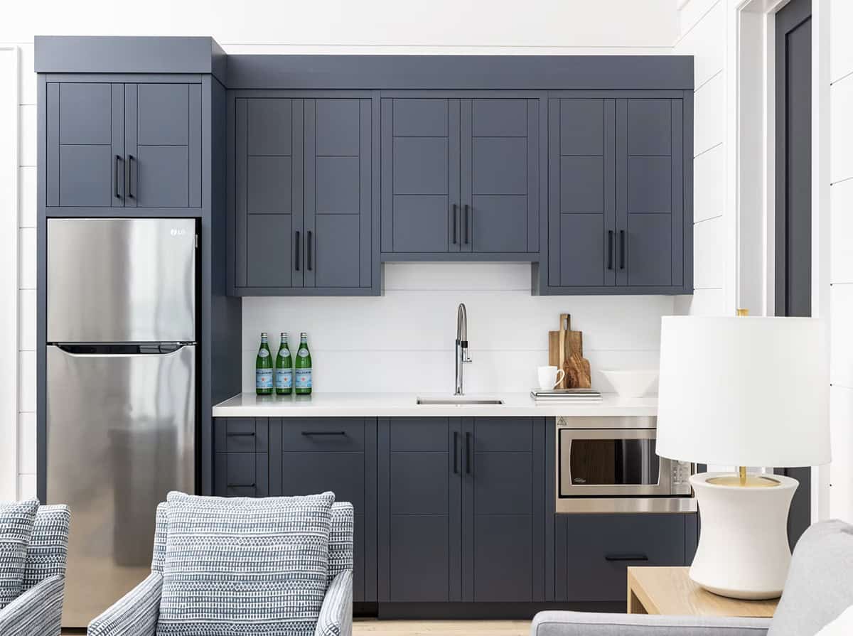 Navy blue shaker-style kitchenette with stainless steel refrigerator, white countertops, and black hardware