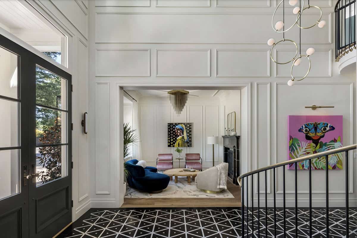 Grand foyer with wainscoting panels, modern chandelier, and view into formal living room with colorful artwork