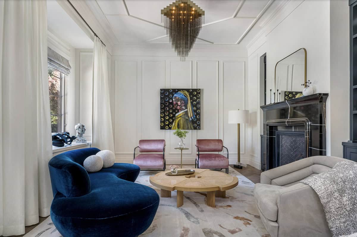 Formal living room with curved navy velvet sofa, dusty rose chairs, organic wood coffee table, and chain chandelier