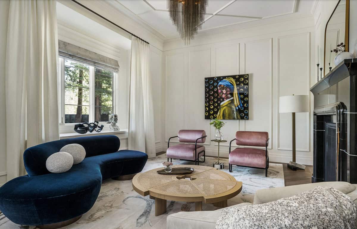 Living room with biomorphic navy sofa, woven round coffee table, and contemporary art above marble fireplace