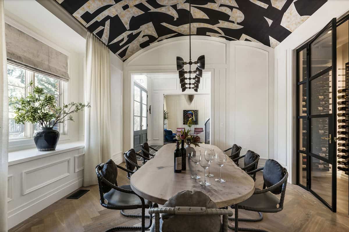 Dining room with barrel-vaulted graffiti-art ceiling, live-edge oval table, and adjacent glass-enclosed wine cellar
