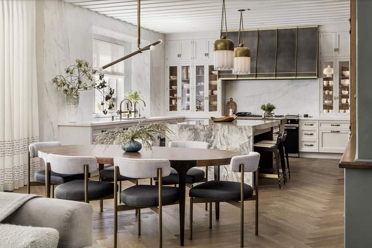 Open-plan kitchen and dining area with marble waterfall island, brass pendant lights, and fluted white ceiling