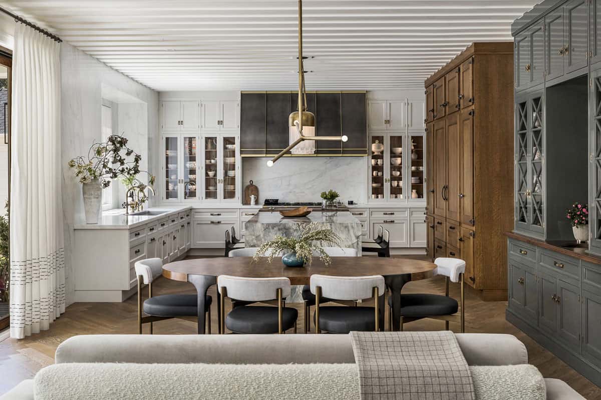 Kitchen with dark range hood, sage green hutch, marble island, and oval walnut dining table with brass-frame chairs