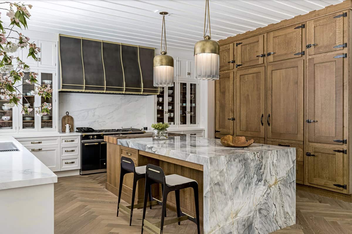 Kitchen featuring dramatic marble waterfall island, dark French range with brass trim, and warm oak pantry cabinet
