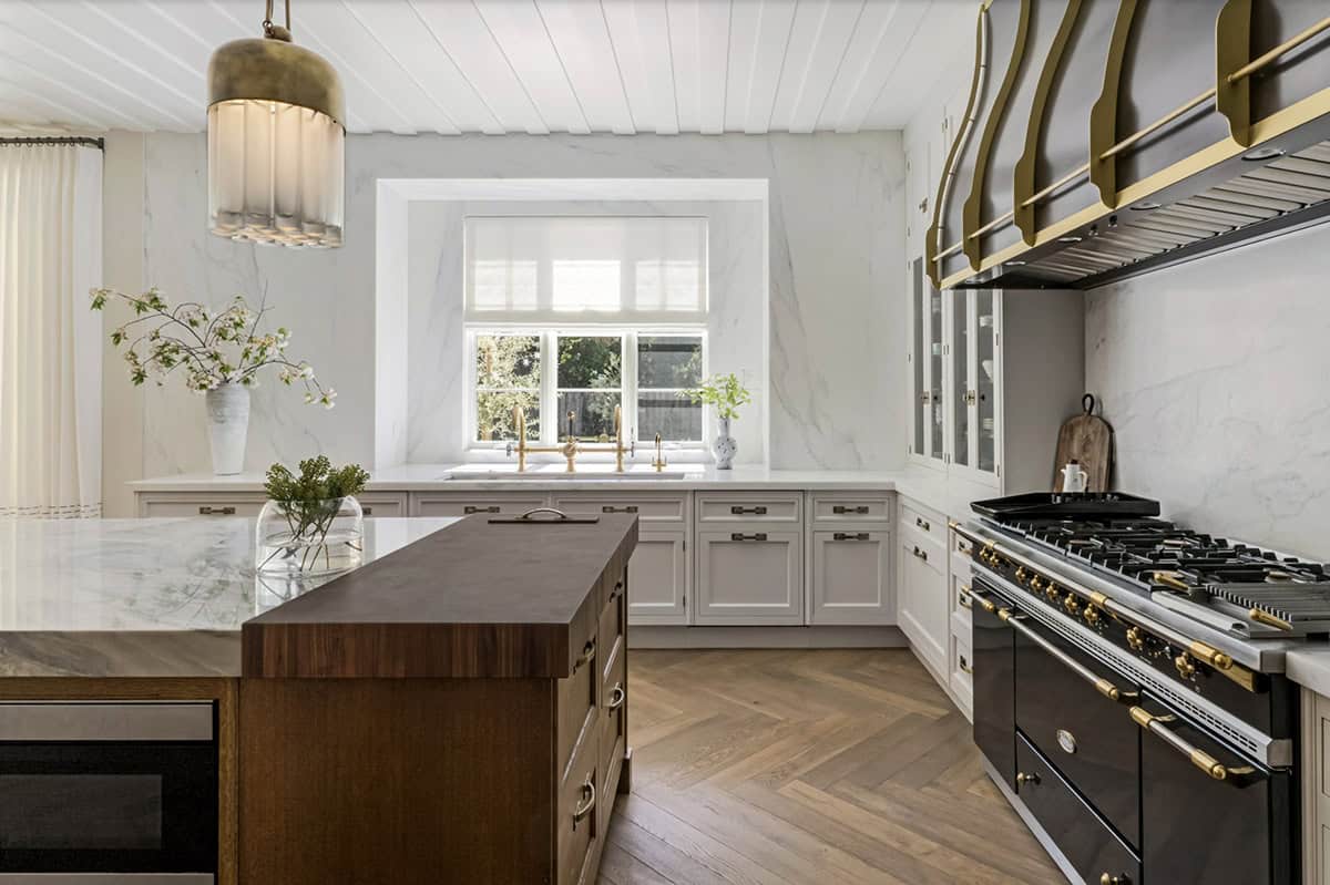 Kitchen sink wall with full marble backsplash, brass bridge faucet, and professional black-and-gold range