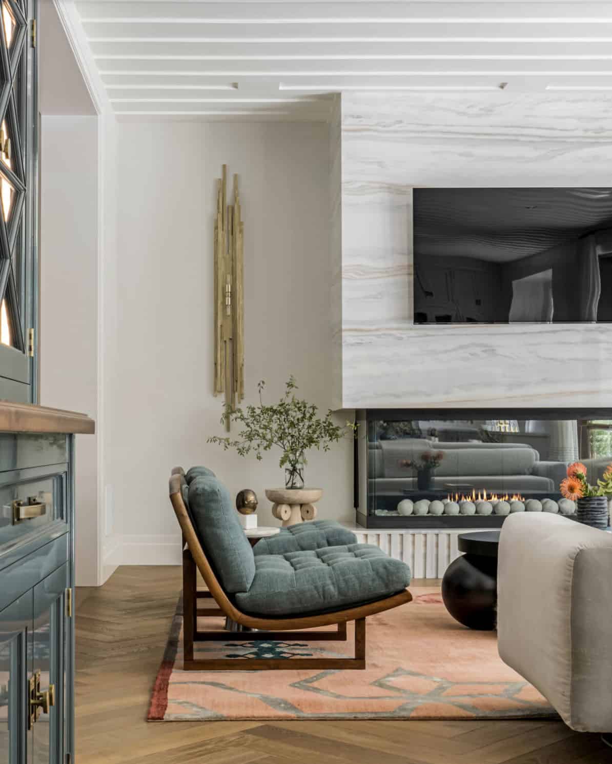 Family room corner with tufted teal lounge chair, see-through linear fireplace, and marble surround